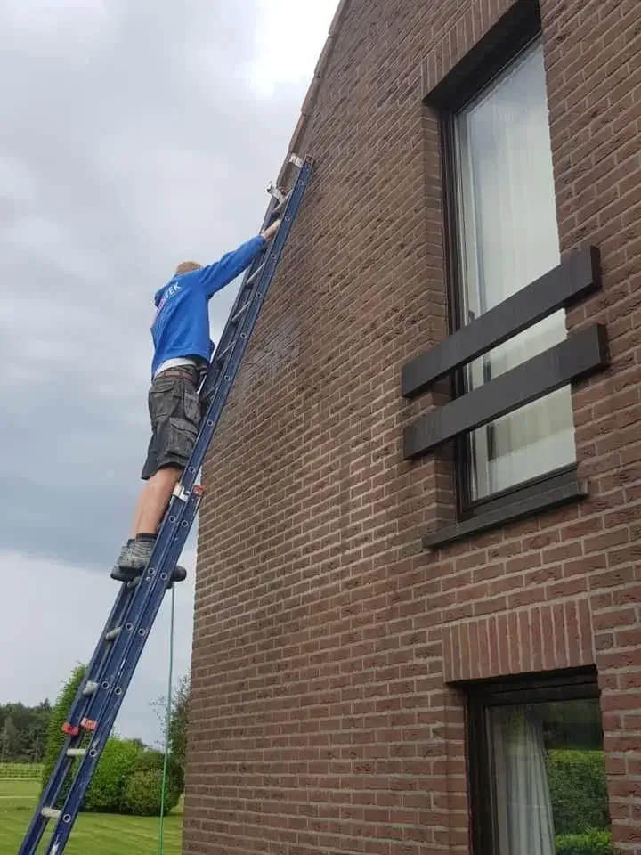 Ouvrier sur une échelle appliquant un hydrofuge sur une façade extérieure pour protection contre l’humidité.