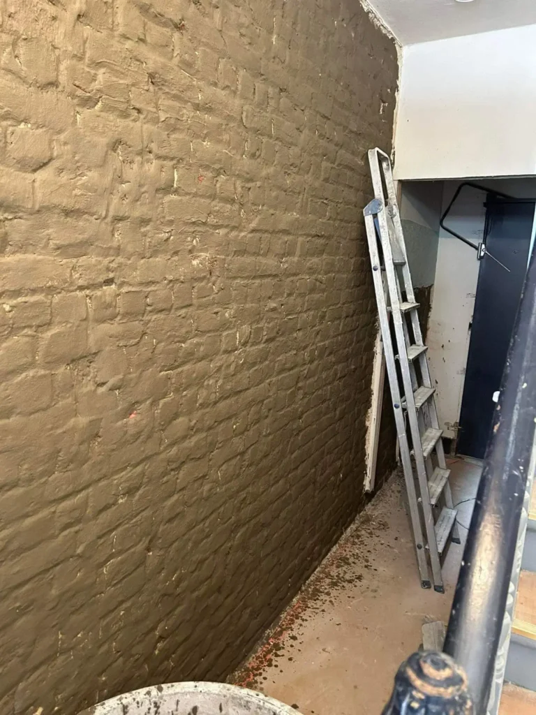 Mur intérieur rénové après traitement de l’humidité, avec enduit neuf appliqué et surface propre prête à être repeinte.