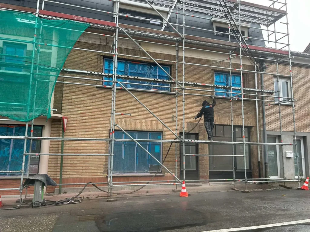 Échafaudage présent à l'avant d'une façade d'une maison avec un ouvrier Humiditek occupé à travailler