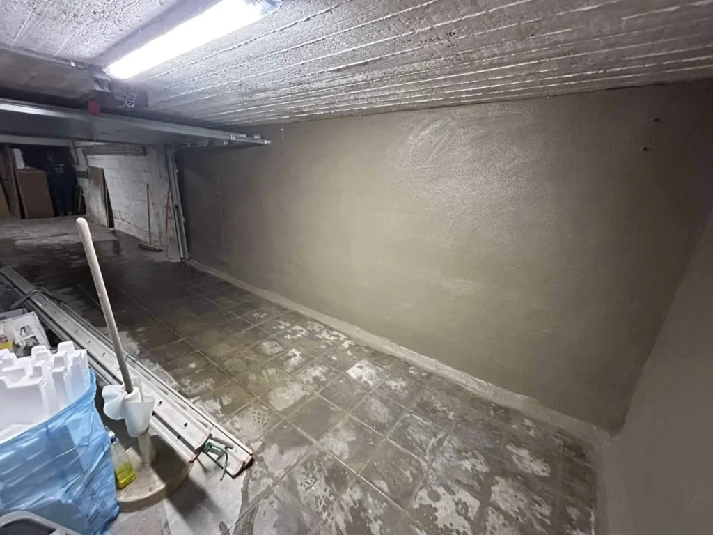Cave humide en cours de traitement, avec murs en pierre partiellement asséchés et sol recouvert d’un revêtement de protection.