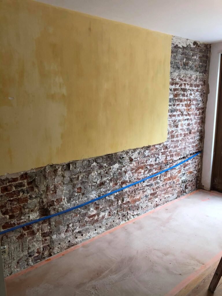 Mur intérieur partiellement décapé en préparation d’un traitement contre l’humidité par injection.
